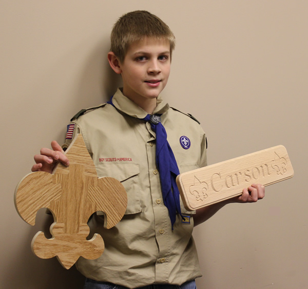 A Scout holding up his emblem puzzle and name plaque