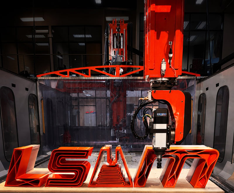 Orange 3D-printed LSAM letters under the trim head of a Thermwood LSAM system